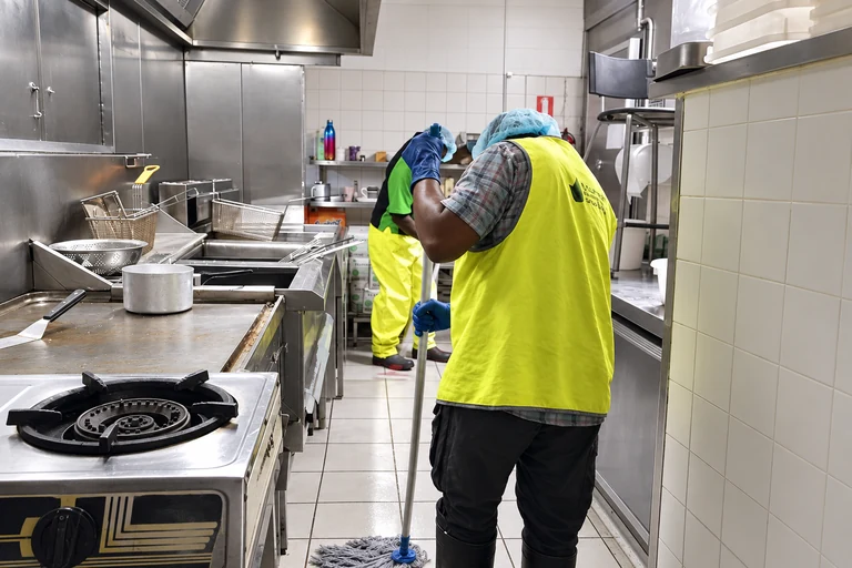 Deux professionnels équipés de gants nettoient le sol d’une cuisine de restaurant